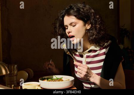 Eine junge Frau mit lockigen Haaren genießt ihr Mittagessen in einem modernen Café, was Muße widerspiegelt Stockfoto