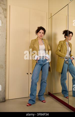 Eine junge Frau mit lockigen Haaren, smart casual gekleidet, posiert in der Nähe eines Spiegels Stockfoto