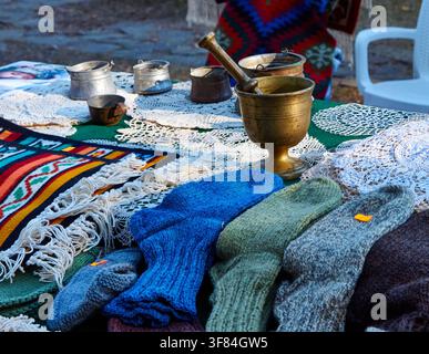 Auslage von farbenfrohen gestrickten Socken, Spitzendecken und vintage Metallbehältern auf einem Tisch bei einem traditionellen bulgarischen Festival in einer Außenumgebung Stockfoto