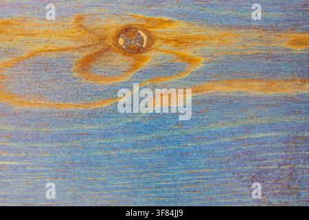 Nahaufnahme-Hintergrundtextur aus horizontaler Holzplatte, die mit blauem und gelbem Lack gestrichen ist und natürliche Maserung sowie zentrale Aststelle für kreatives Design zeigt. Stockfoto