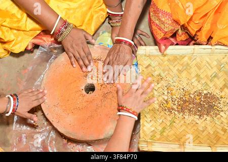 Indische Frauenhände mahlen Getreide auf einer traditionellen Steinhandmühle Chakki während eines hinduistischen religiösen Rituals und eines festlichen Festes im ländlichen Indien. Stockfoto