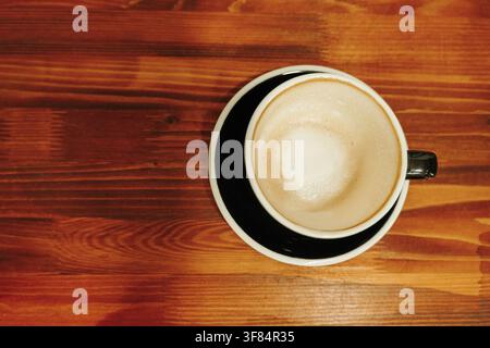 Oberansicht eines frisch zubereiteten Cappuccinos mit cremigem Milchschaum auf einem Holztisch. Minimale Kaffeekomposition mit Kopierraum. Stockfoto