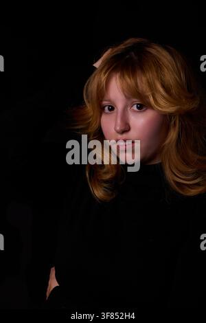 Junge Frau mit rotem Haar blickt auf schwarzem Hintergrund in die Kamera Stockfoto