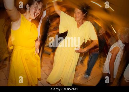 zwei Frauen tanzen fröhlich in gelben Kleidern auf einer Indoor-Party mit Keramikfliesenboden, Augenhöhe. Stockfoto