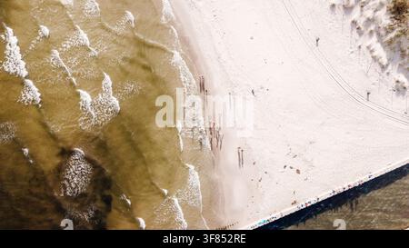 Luftaufnahme von oben eines sandigen Strandes mit Meereswellen und langen Schatten von Menschen Stockfoto