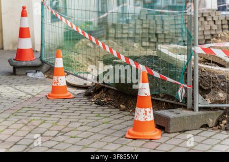 Baubarriere mit orangefarbenen reflektierenden Verkehrskegeln, schützendem Maschendrahtzaun und Warnband, das städtische Subgrade-Aushub sichert Stockfoto