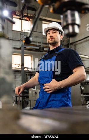 Selbstbewusster Industriearbeiter steht neben Maschinen in der Fabrik Stockfoto