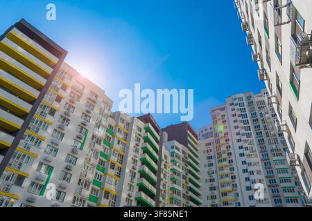 Aufblick auf neu fertiggestellte mehrstöckige Wohnkomplexgebäude unter einem hellen klaren blauen Himmel mit Lichtsprengung von der Sonne in einem städtischen Viertel Stockfoto
