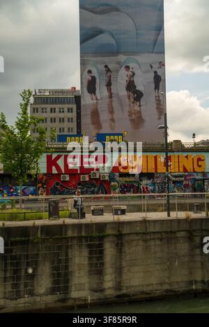 Wien, Österreich - 10. Juni 2023: Großes Wandgemälde an einer Gebäudefassade am Wiener Ufer, das Menschen am Strand zeigt, mit dem Graffiti-Text 'Keep Smiling' Stockfoto