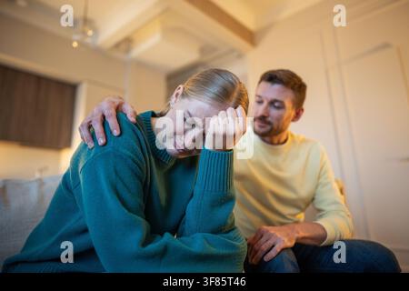 Verheiratetes Paar sitzt nach Streit zusammen auf der Couch, weinende Frau distanziert sich von ungerechtem Ehemann Stockfoto