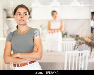 Das beleidigte Mädchen sitzt am Tisch in der Küche und hört zu, wie die Frau sie beschimpfte Stockfoto