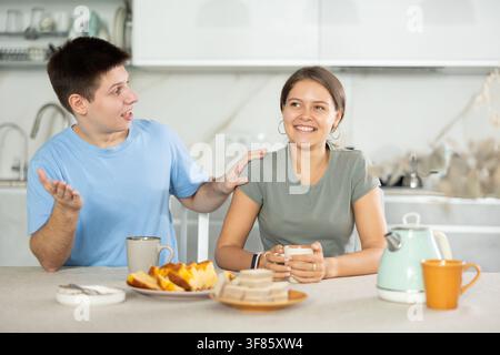 Glückliches junges Paar, das am Küchentisch sitzt und sich beim Tee unterhalten kann Stockfoto