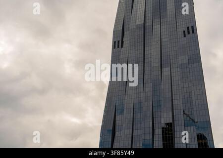 Moderner Glas- und Stahl-Wolkenkratzer in Wien, Österreich, von unten gegen einen bewölkten Himmel aufgenommen. Zeitgenössische Architektur mit vertikal gerippter Fassade de Stockfoto