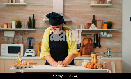 Der Backprozess setzt sich mit sorgfältigem Handkneten auf dem Tisch fort, bevor der Teig geformt wird, an einem für das Heimbacken vorbereiteten Tisch vor dem Brotbacken. Stockfoto