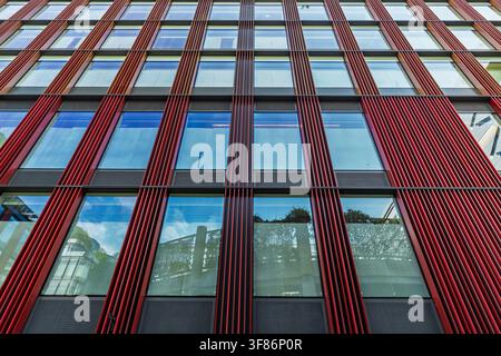 Ansicht der modernen Glasfassade eines Gebäudes in der City of London mit auffälligen roten vertikalen Lamellen und reflektierenden Fenstern in London, England, Un Stockfoto