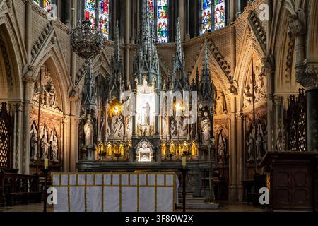 Verzierter neugotischer Hochaltar und geschnitzter Rückwandaltar unter bunten Buntglasfenstern in St. Colmans Kathedrale, Cobh, County Cork, Irland Stockfoto