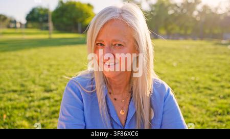 Seniorin lächelt in einem sonnigen grünen Park Stockfoto