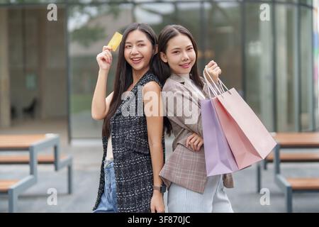 Zwei asiatische Frauen halten Einkaufstüten und Kreditkarten im Freien für die Black-Friday-Verkaufsförderung Stockfoto