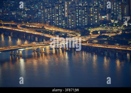Telefoto-Nachtaufnahme eines komplexen Autobahnkreuzes und einer Brücke über den Han-Fluss in Seoul mit Wasserreflexionen. Stockfoto