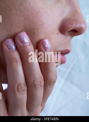Frau posiert mit einer Nahaufnahme ihres Gesichts und eines manikürten Fingers, um natürliche Schönheit zu zeigen. Stockfoto