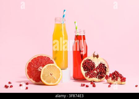 Frische Fruchtsäfte in Glasflaschen mit Grapefruit, Zitrone und Granatapfel auf einem rosa Hintergrund Stockfoto