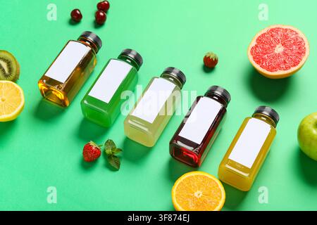 Sortiment an farbenfrohen Obst- und Gemüsesäften in klaren Flaschen mit leeren Etiketten auf grünem Hintergrund Stockfoto