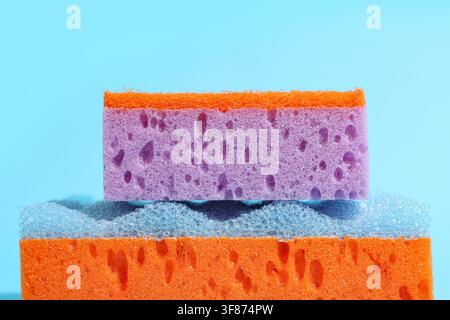 Stapel bunter Reinigungsschwämme mit einem violetten Schwamm oben auf einem blauen und orangefarbenen Schwamm, die Schwämme zeigen ihre poröse Struktur und sind platziert Stockfoto