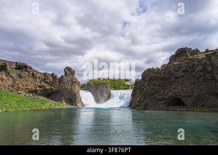 Panoramablick auf den Hjalparfoss-Wasserfall, der zwischen einzigartigen Basaltfelsen in ein klares, türkisfarbenes Becken in der Thjorsardalur-Schlucht in Island stürzt Stockfoto