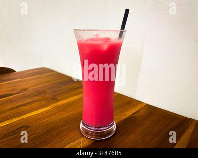 Eisgetränk mit rosa Farbe und Strohhalm auf einem Holztisch in einem Café Stockfoto