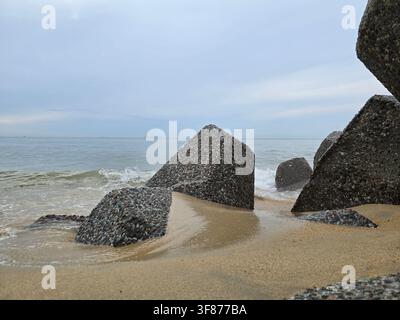 Große strukturierte Beton-Pfeilerblöcke ruhen auf einem sandigen Strand und schützen die Küstenlinie vor Ozeanwellen. Stockfoto