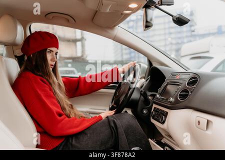 Frau Auto fahren stilvolle Dame mit rotem Barett und Pullover sitzt auf dem Fahrersitz einer modernen Fahrzeugkabine am Tag Stockfoto