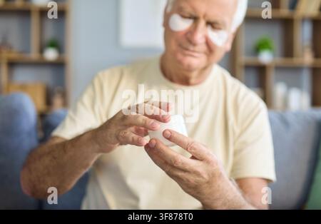 Senior applies Creme mit Unteraugen-Patches zu Hause für Hautpflege-Wellness Stockfoto
