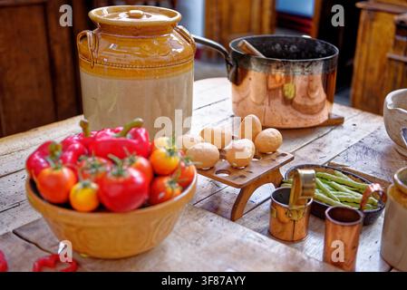 Eine wunderschön inszenierte kulinarische Darstellung mit frischen Tomaten, Paprikaschoten, Eiern auf einem Holzregal und Kupfertöpfen auf einer rustikalen Holzoberfläche Stockfoto