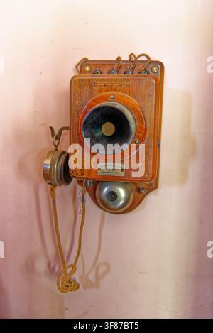 Ein seltenes historisches Wandtelefon aus Holz mit einer Messingglocke, Mikrofonlautsprecher und einem hängenden Seitenempfängerteil im Lanhydrock House, Cornwall, am Stockfoto