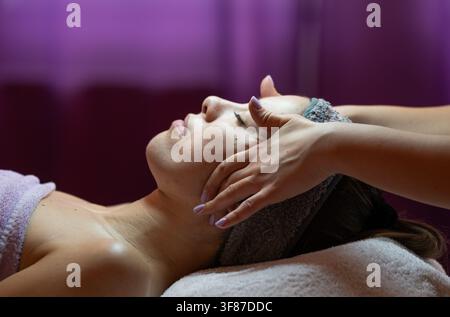 Junge Frau liegt auf einem Spa-Bett und erhält eine entspannende Gesichtsbehandlung von einer professionellen Kosmetikerin. Schönheitstreatment mit Fokus auf Wellness, Hautpflege Stockfoto