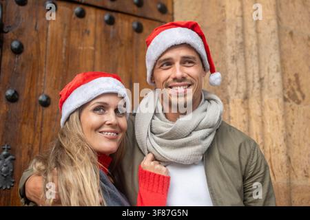 Lächelndes Paar trägt Weihnachtsmützen und warme Kleidung und genießt Weihnachten zusammen im Freien in der Stadt. Stockfoto