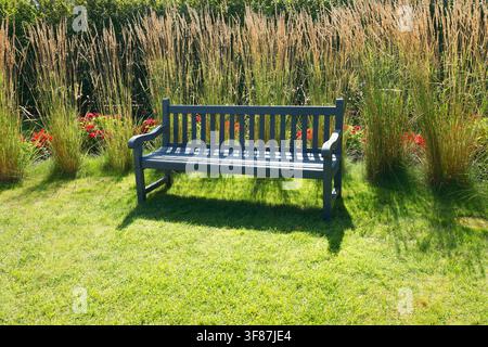 Graue Holzbank in trockenem Ziergras. Modernes nachhaltiges Cottage-Garten-Rewilding-Designkonzept. Ästhetisches trockenresistentes Sommerhinterhof Stockfoto
