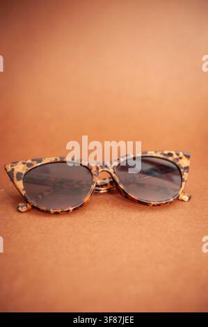 Schildpatt-Cat-Eye-Sonnenbrille, die auf einer warmen braunen Oberfläche ruht, mit weichem Hintergrundunschärfeeffekt und großzügigem Kopierraum Stockfoto