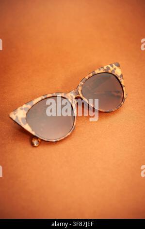 Schildpatt-Cat-Eye-Sonnenbrille, die auf einer warmen braunen Oberfläche ruht, mit weichem Hintergrundunschärfeeffekt und großzügigem Kopierraum Stockfoto