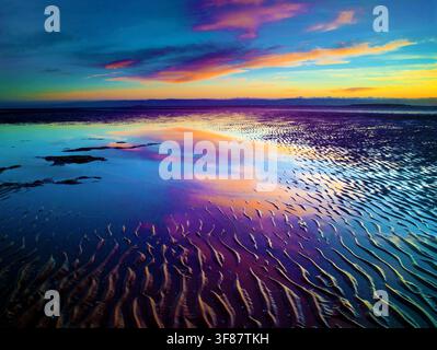 Sonnenuntergangsreflexionen auf nassem, welligem Sand bei Ebbe. Stockfoto
