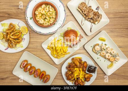 Überkopf-Tapas-Platte mit Knoblauchgarnelen, Calamari, Kroketten, Burger, Hühnerflügeln und Garnelen-Toast Stockfoto