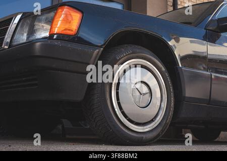 Lindau, Schweiz, 9. August 2026. Niederwinkel-Nahaufnahme des Vorderrads, des klassischen Mercedes-Stern-Radkappen und des Kotflügels eines W124 E-Klasse-Modells aus den 1990er Jahren. Stockfoto