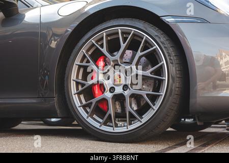 Lindau, Schweiz, 9. August 2026. Niedrigwinklige Nahaufnahme, die ein mehrspeichiges dunkelgraues Aluminiumrad, eine Porsche-Krone als Mittelkappe und einen roten Bremszangen zeigen Stockfoto