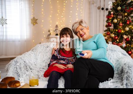 Großmutter und Enkelin sitzen auf dem Sofa und lächeln während Weihnachten Stockfoto