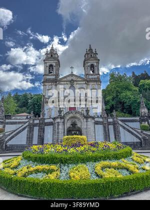 Die Bom Jesus do Monte-Grand-Kirche erhebt sich hoch mit zwei Glockentürmen und verzierter Fassade. Der blaue Himmel mit flauschigen Wolken kontrastiert mit der Steinarchitektur. Lu Stockfoto