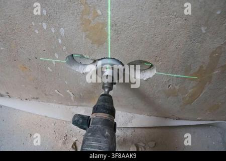 Arbeiter bohrt Löcher in eine Betonwand mit einem leistungsstarken Bohrhammer und Lochsägenaufsatz, wobei er einen grünen Laserlevel für eine präzise Positionierung verwendet, duri Stockfoto