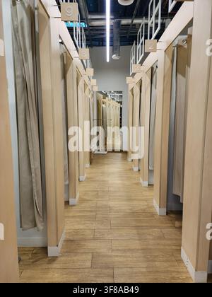 Leerer Umkleidekorridor in einem Einzelhandelsgeschäft mit Reihen von einzelnen Umkleidekabinen mit heller Holzvertäfelung, beigefarbenen Vorhängen und nummerierten Sitzen Stockfoto