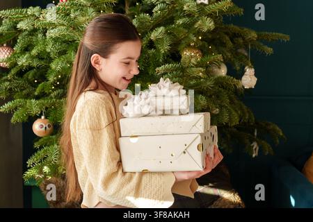 Teenage-Mädchen trägt gestapelte Weihnachtsgeschenke neben einem geschmückten Baum Stockfoto