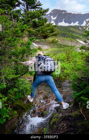 Wandererin mit einem Rucksack klettert durch die Felsen auf dem Bergpfad mit einem Wasserbach im Frühling. Stockfoto