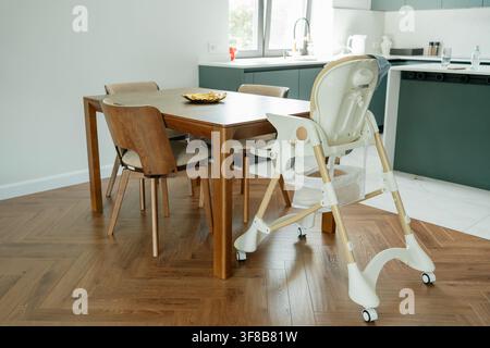 Essbereich mit hölzerner Essgruppe und verstellbarem Kinderhochstuhl in der Nähe der Küche in einer modernen Wohnung. Perfektes Bild für Familienleben, Interieur Stockfoto